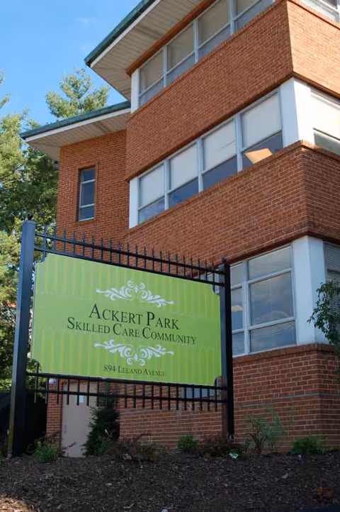 Brick exterior of a building with a green Ackert Park sign by the entrance.