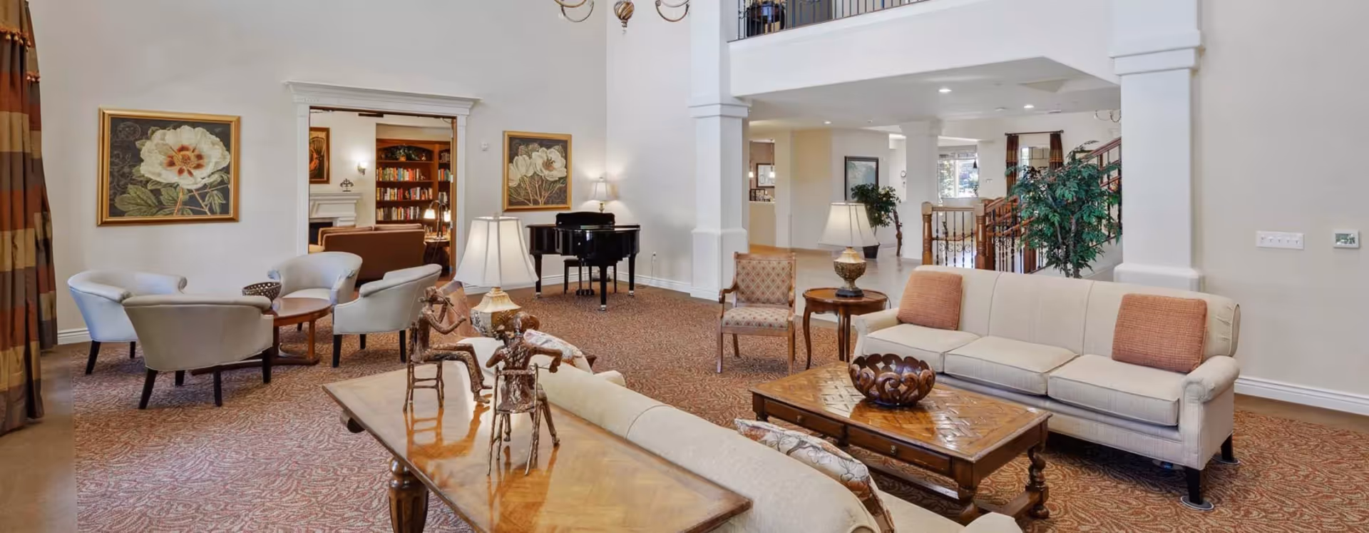 Spacious furnished senior living lounge with sofas, armchairs, coffee tables, artwork, and a piano in an open, carpeted room.