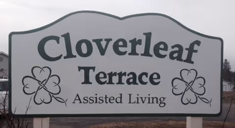 A large Cloverleaf Terrace Assisted Living sign with shamrock decorations outdoors.