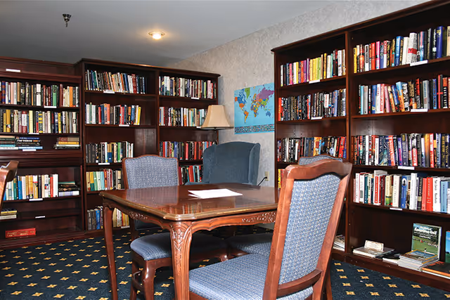 A cozy interior reading room with wooden bookshelves, a table and upholstered chairs.