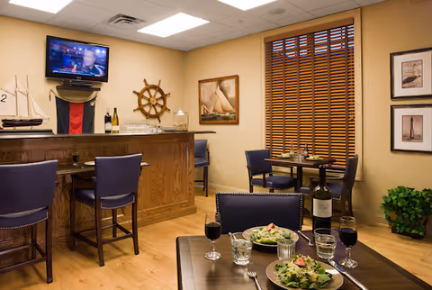 Small dining and bar area with tables set with salads and wine, nautical decor, and a wall-mounted TV.