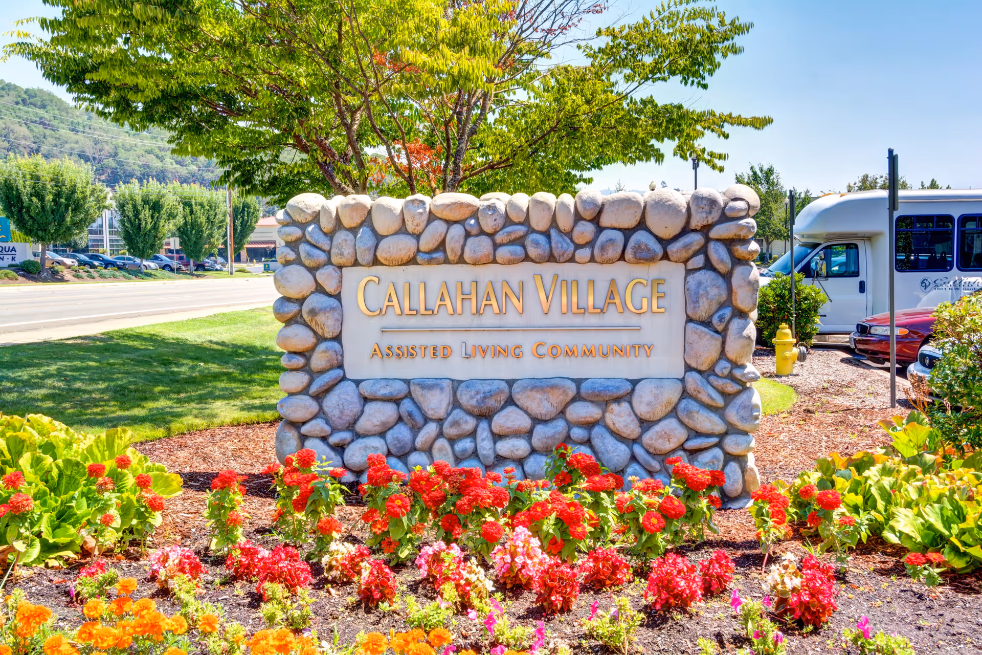 Stone entrance sign that reads "Callahan Village Assisted Living Community" set among flowers and landscaping.