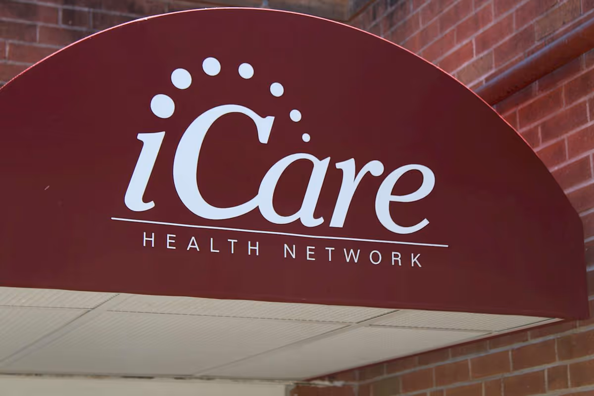 A maroon awning with the white text 'iCare Health Network' printed on it, attached to a brick building.