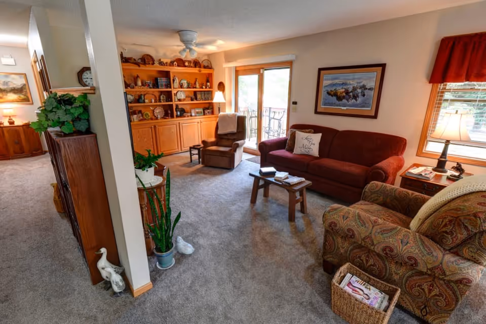 Cozy living room with a red sofa, patterned armchair, recliner, wooden coffee table, built-in shelving, and sliding glass doors to a balcony.