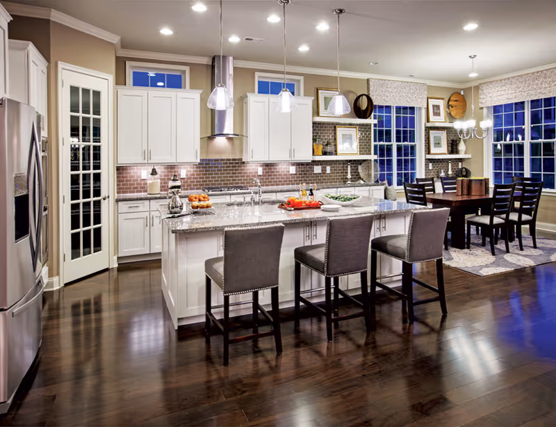 Open-concept kitchen with a large island, three bar stools, stainless steel appliances, and an adjacent dining table.