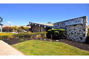 Exterior view of Bay View Nursing & Rehab Center building with a stone facade and a sign displaying the facility's name. The foreground features a well-maintained lawn, trimmed bushes, and a clear blue sky.