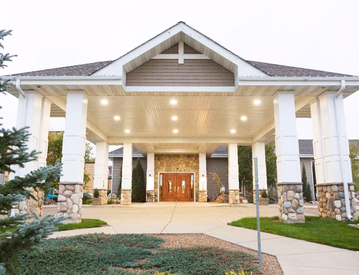 Covered porte-cochère entrance with white columns and stone bases leading to double wooden doors of the facility.