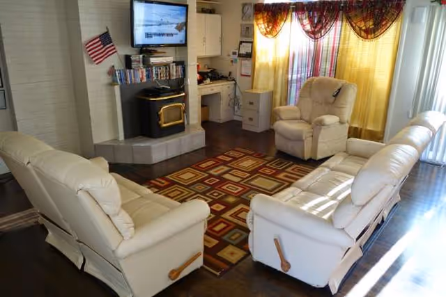 Cozy living room with white leather sofas, a fireplace, TV, and colorful curtains.