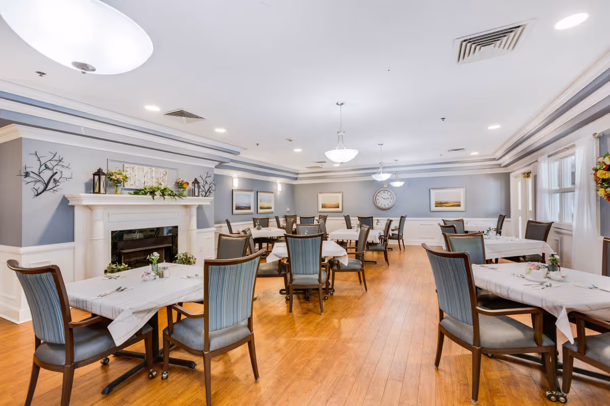 Spacious dining room with multiple set tables and chairs, a decorative fireplace, wall art and overhead pendant lights.