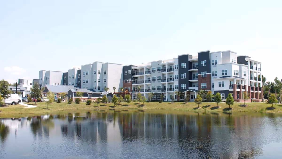 Exterior view of The Savoy Gracious Retirement Living, a modern multi-story senior facility beside a pond.