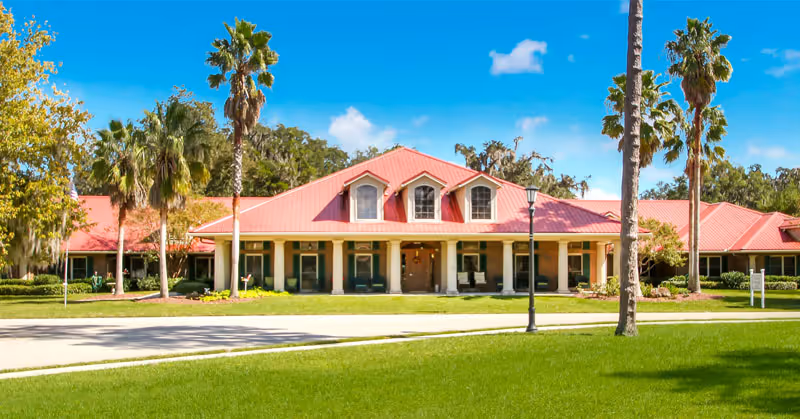 Single-story red-roofed building with columns and palm trees on a manicured lawn under a blue sky.