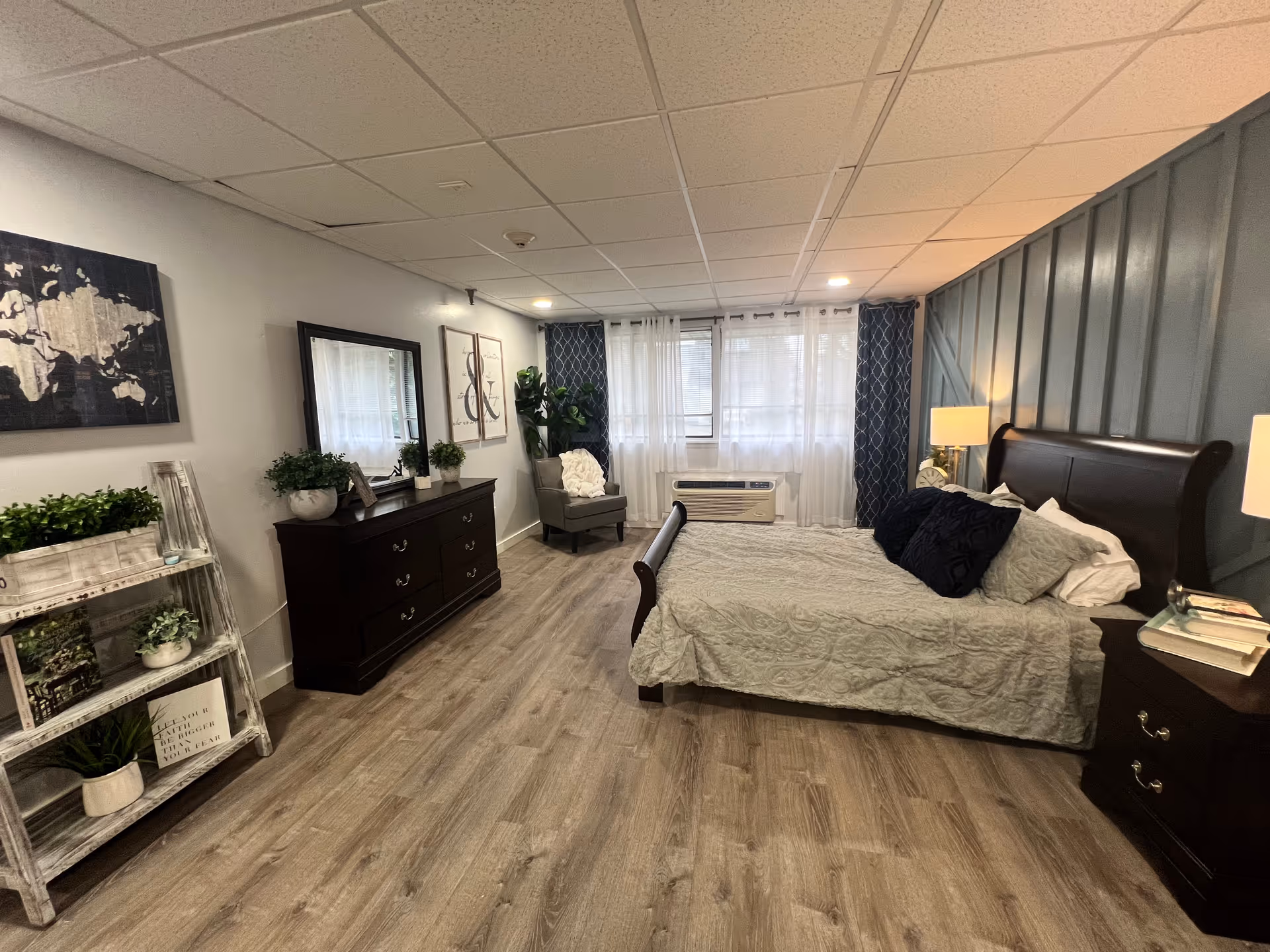 Spacious bedroom with a large bed, dark wood furniture, and sheer-curtained window.