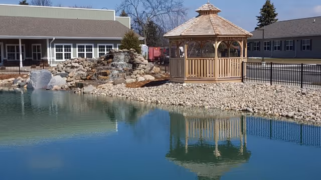 Outdoor pond with rock waterfall and wooden gazebo at Traditions of Saginaw West Campus