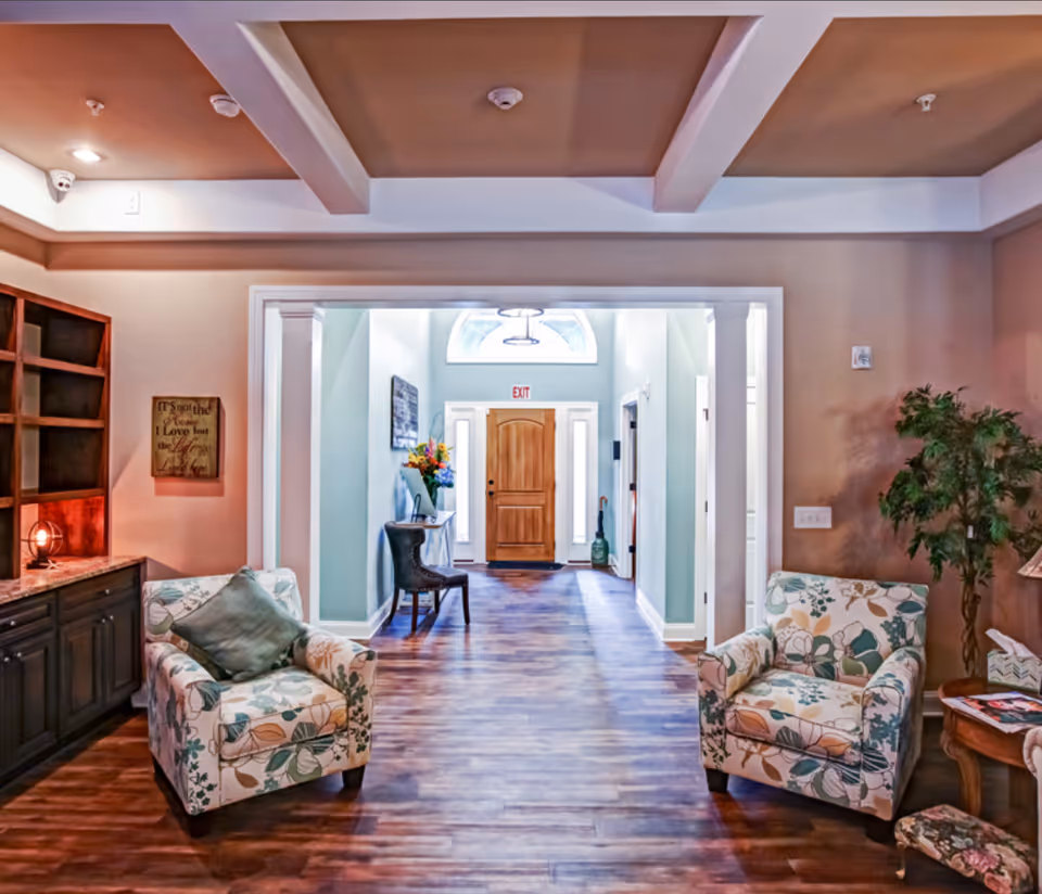 Bright common lounge with two patterned armchairs, built-in shelving, and a hallway leading to a wooden door.