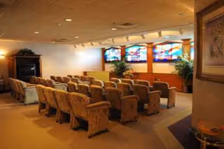 A small auditorium-style room with rows of upholstered chairs facing a wall with decorative stained-glass windows and an entertainment cabinet.
