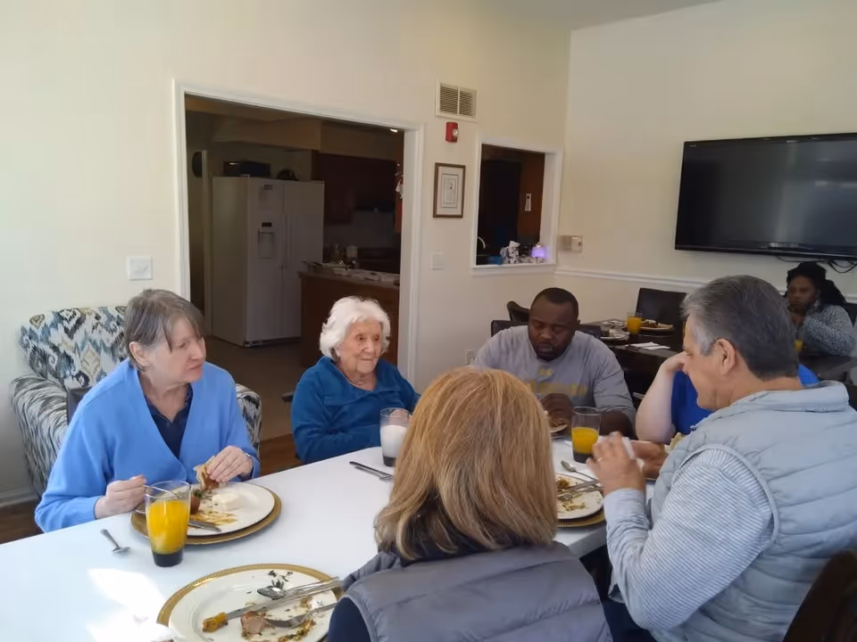 Several residents and staff seated around a dining table having a meal in a communal room.
