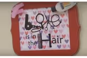 Wall decor sign with hearts that reads "Love is in the Hair" decorated with scissors, a comb, and a hair product.