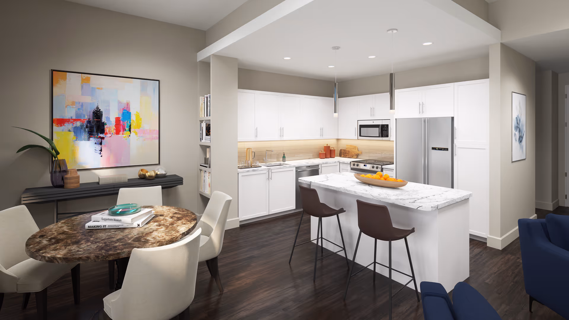 Modern kitchen and dining area in a senior living facility with white cabinets, stainless steel appliances, a marble countertop island with two brown bar stools, a round dining table with four beige chairs, colorful abstract artwork on the wall, and dark wood flooring.