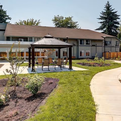 Outdoor courtyard at Firwood Gardens featuring a covered gazebo with chairs, landscaped lawns, and a two-story building in the background.