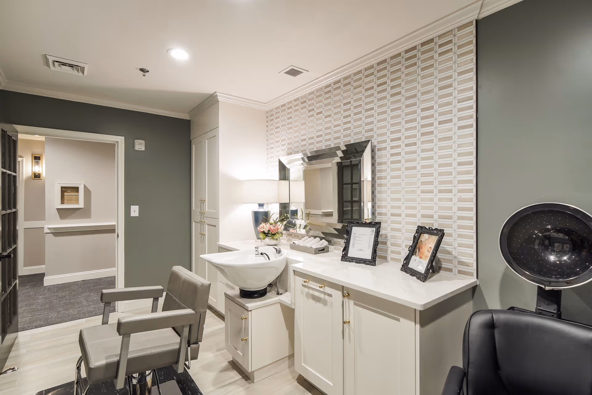 An interior salon area with styling chairs, a wash basin, vanity counter with mirror and a hooded hair dryer.