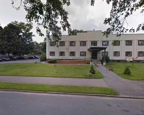 Front view of a two-story beige senior living facility with entrance and lawn.