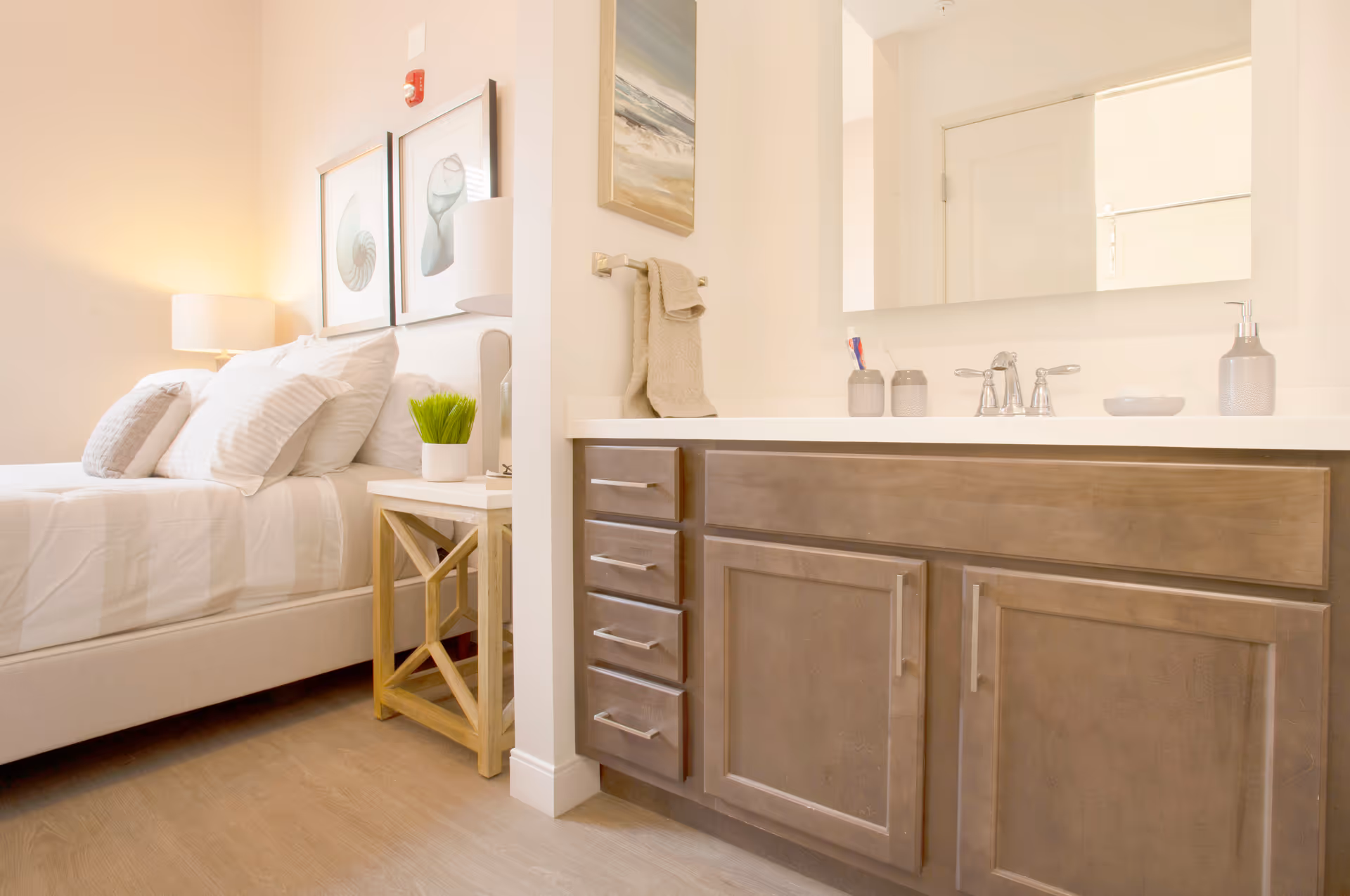 Bright bedroom with a bedside table and lamp next to an adjoining bathroom vanity with sink and mirror.