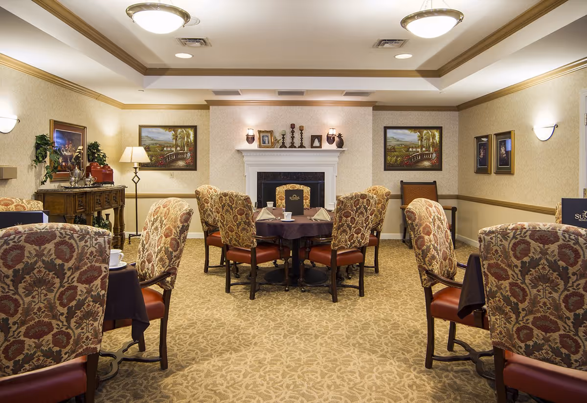 Cozy dining room with round tables and patterned upholstered chairs arranged around a central fireplace.