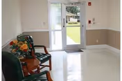 Small bright entryway with two green chairs and a small table beside a glass door leading outside.