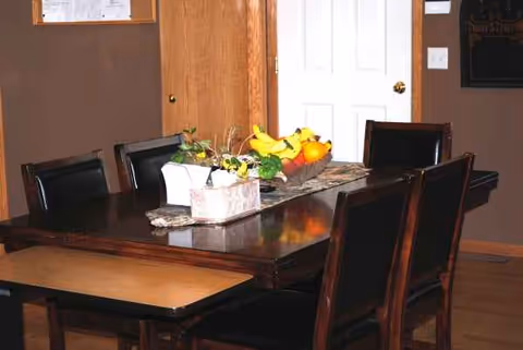 A dark wooden dining table with six chairs and a fruit centerpiece in a dining room.