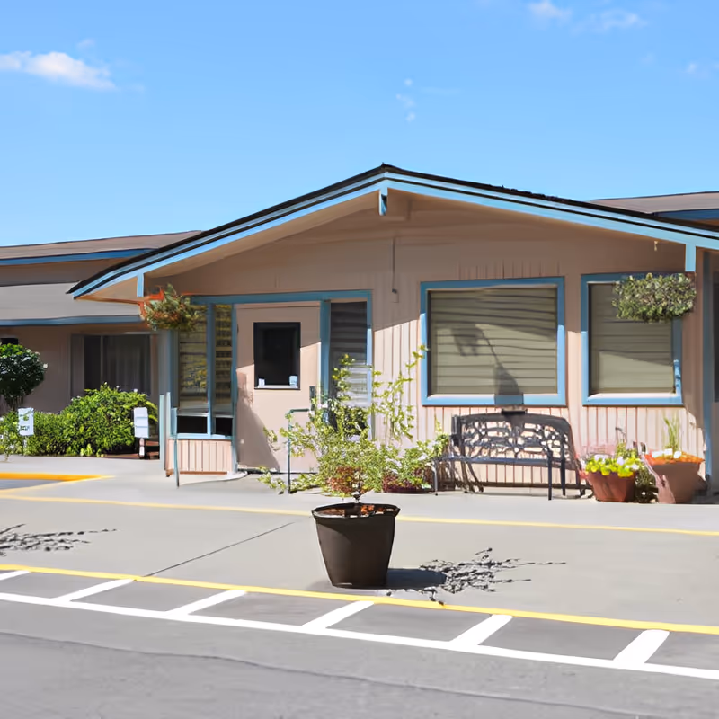 Front entrance of a single-story rehabilitation center with a bench, potted plants, and large windows.