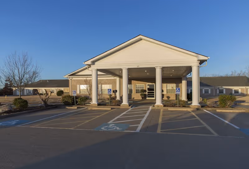 Front exterior of a nursing and rehabilitation center with a covered entrance supported by white columns and marked handicap parking spaces in front.