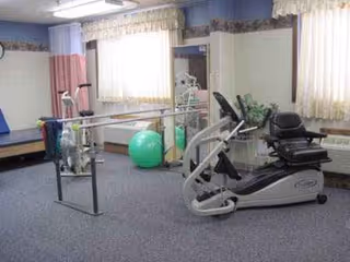 Indoor rehabilitation room with stationary bike, balance bars, and a large green exercise ball.