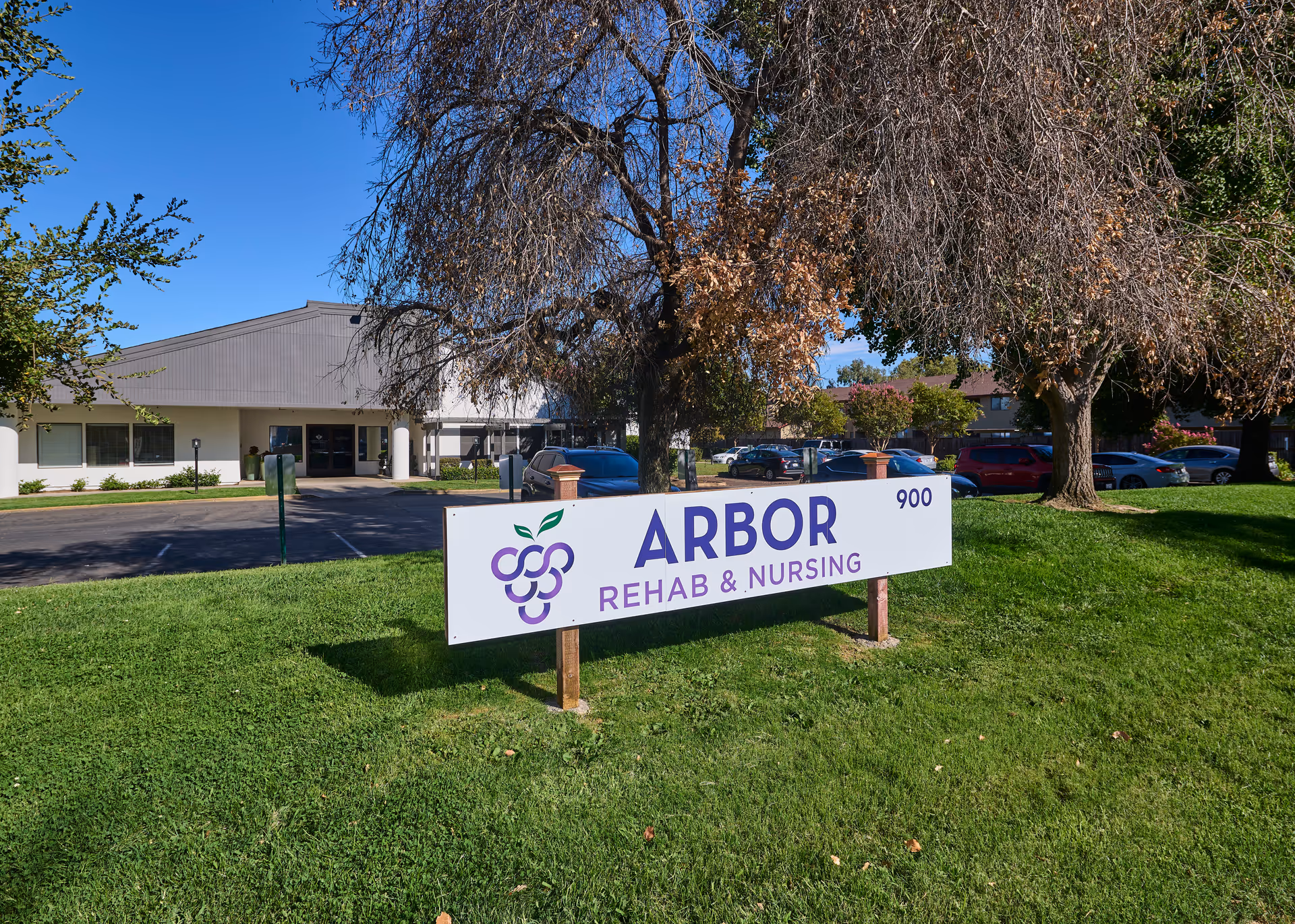 Front exterior of Arbor Rehab & Nursing center with a lawn sign reading 'ARBOR REHAB & NURSING' and the building and trees in the background.