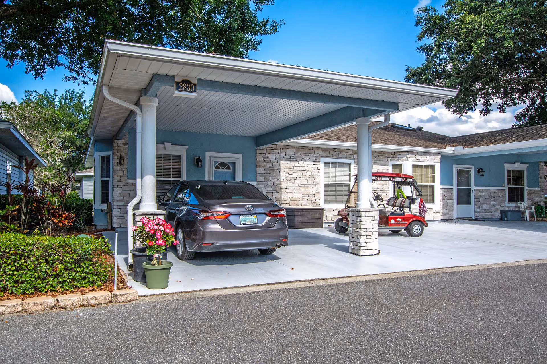 Front exterior of The Oaks at Waterman Village with a carport, parked car, and golf cart.