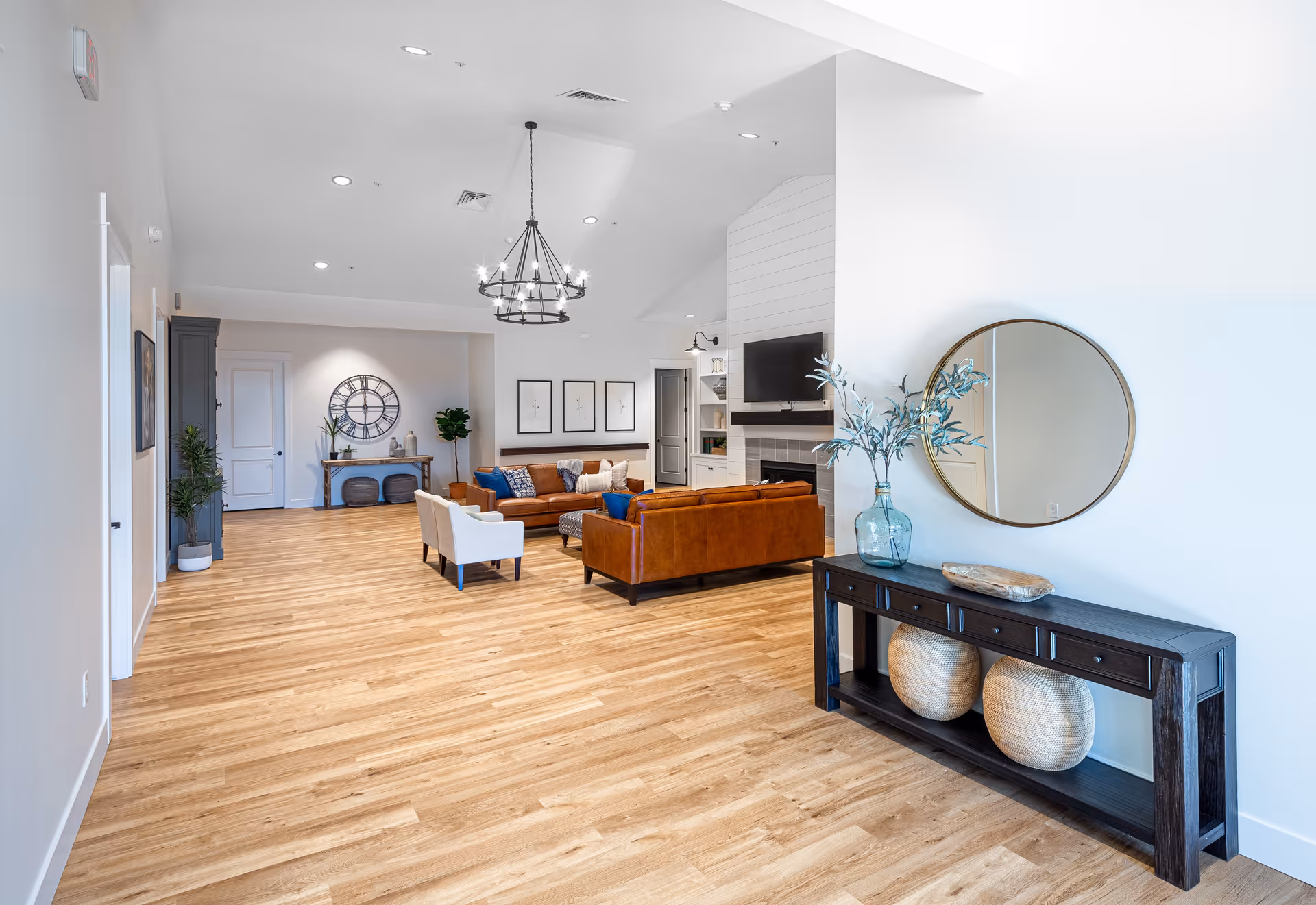 Bright open communal living room with leather sofas, armchairs, a fireplace and a console table topped by a round mirror.