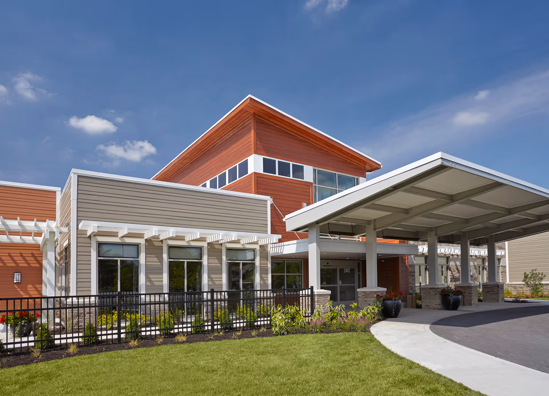 Front entrance of a modern senior living building with a covered drop-off, large windows, and landscaped lawn.
