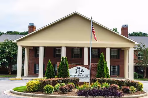 Front exterior of a brick senior living facility with columns and the American flag.
