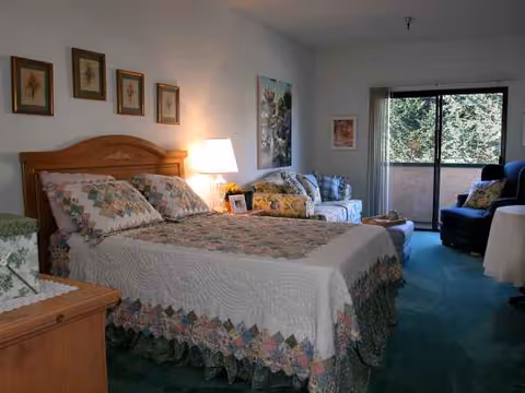 Cozy bedroom in senior living with quilted bed, seating area, and balcony view.