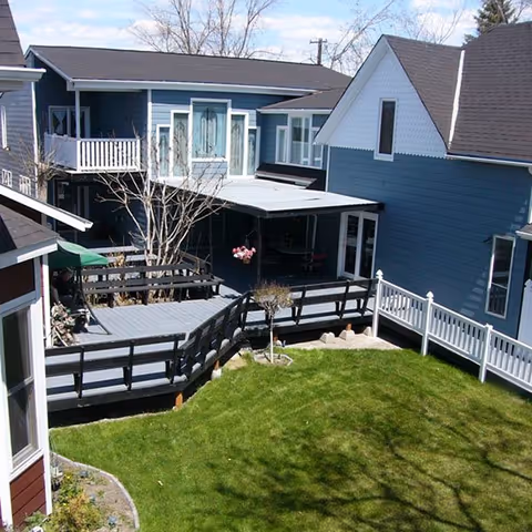 Blue multi-unit building with wooden decks, railings, stairs, and a grassy yard.