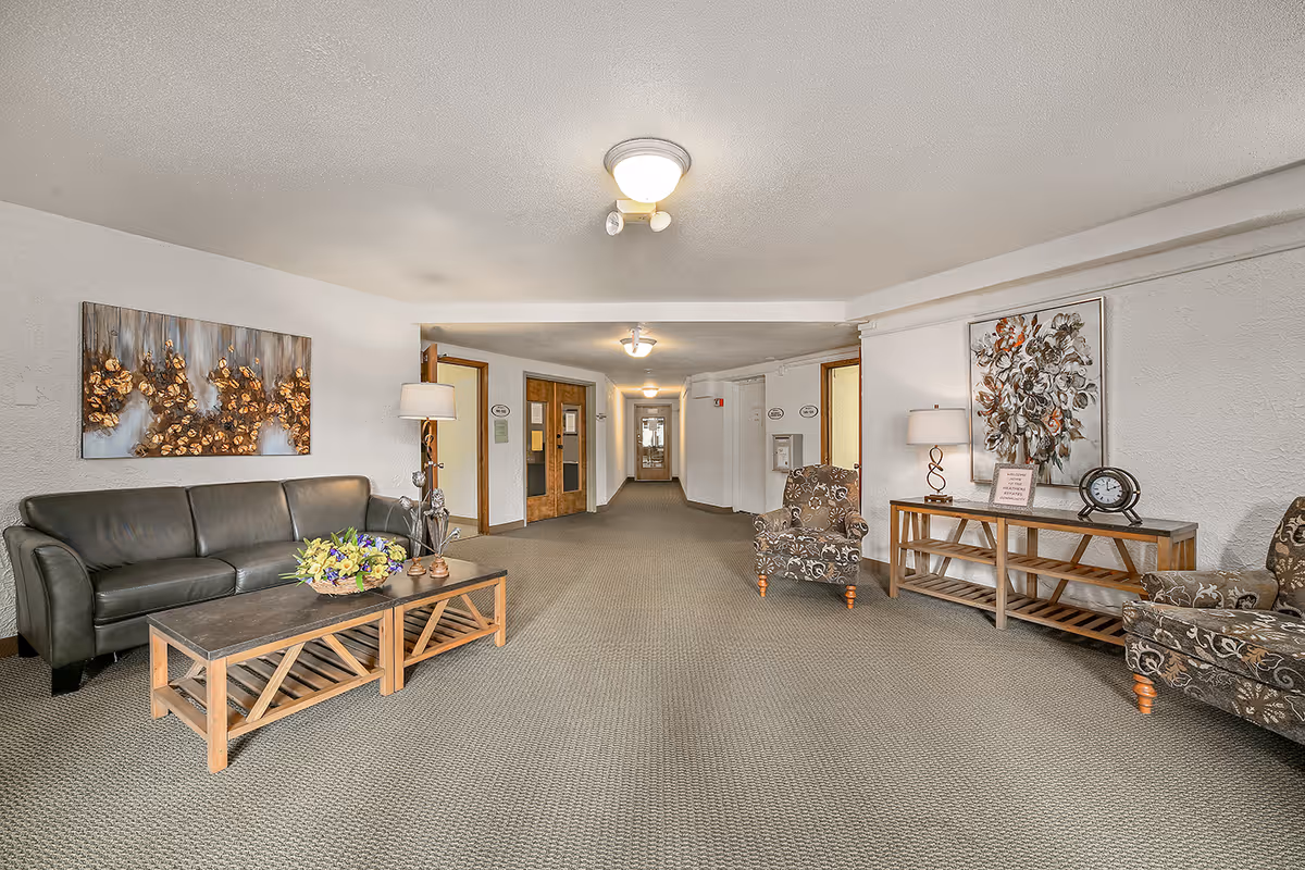 Spacious furnished seating area and hallway in a senior living facility with couches, armchairs, coffee tables and wall artwork.