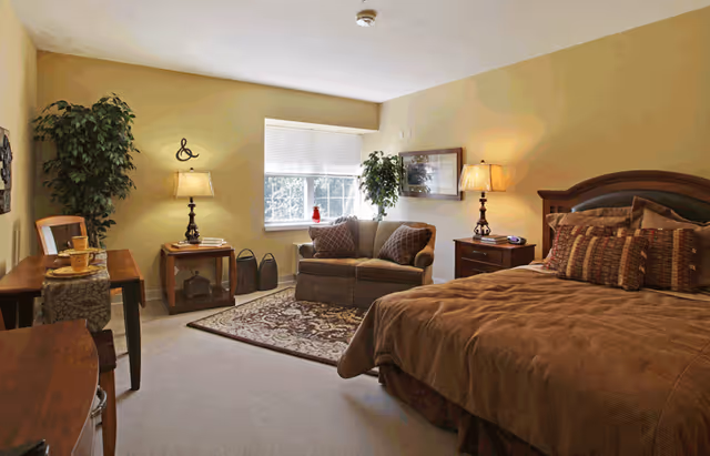 Warmly decorated bedroom with a large bed, a loveseat by the window, two lamps on nightstands, a rug, and a small table.