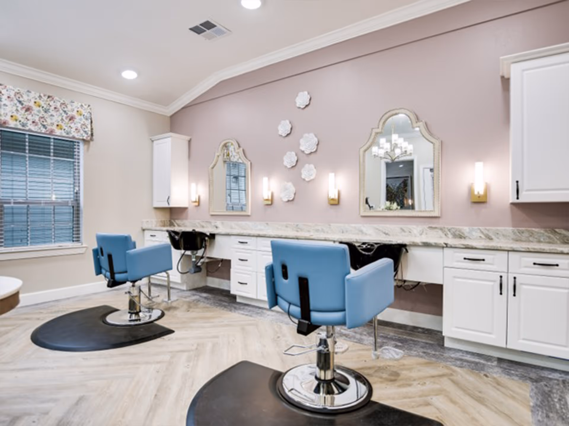 Interior salon area with blue styling chairs, mirrors, and white cabinets along a pink accent wall.