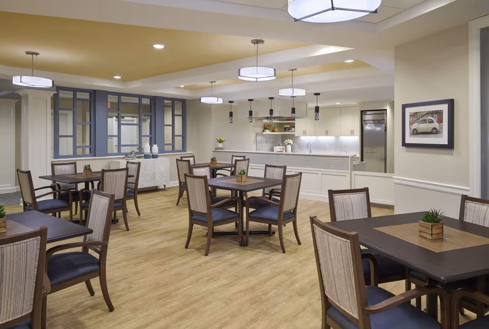 Spacious dining room with multiple wooden tables and chairs and an open kitchen area in the background.