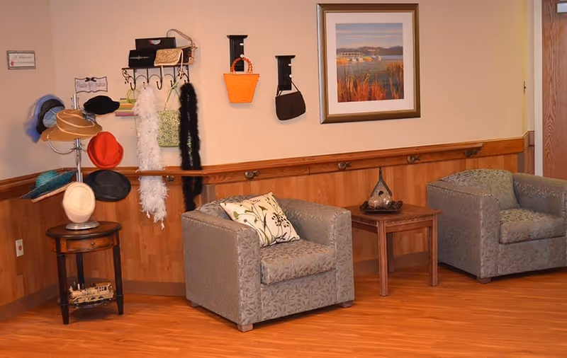 Cozy seating area with two upholstered chairs, a small side table, a hat rack and wall art in a common room.