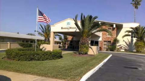 Front entrance of Sandalwood Rehabilitation and Nursing Center with palm trees and an American flag.
