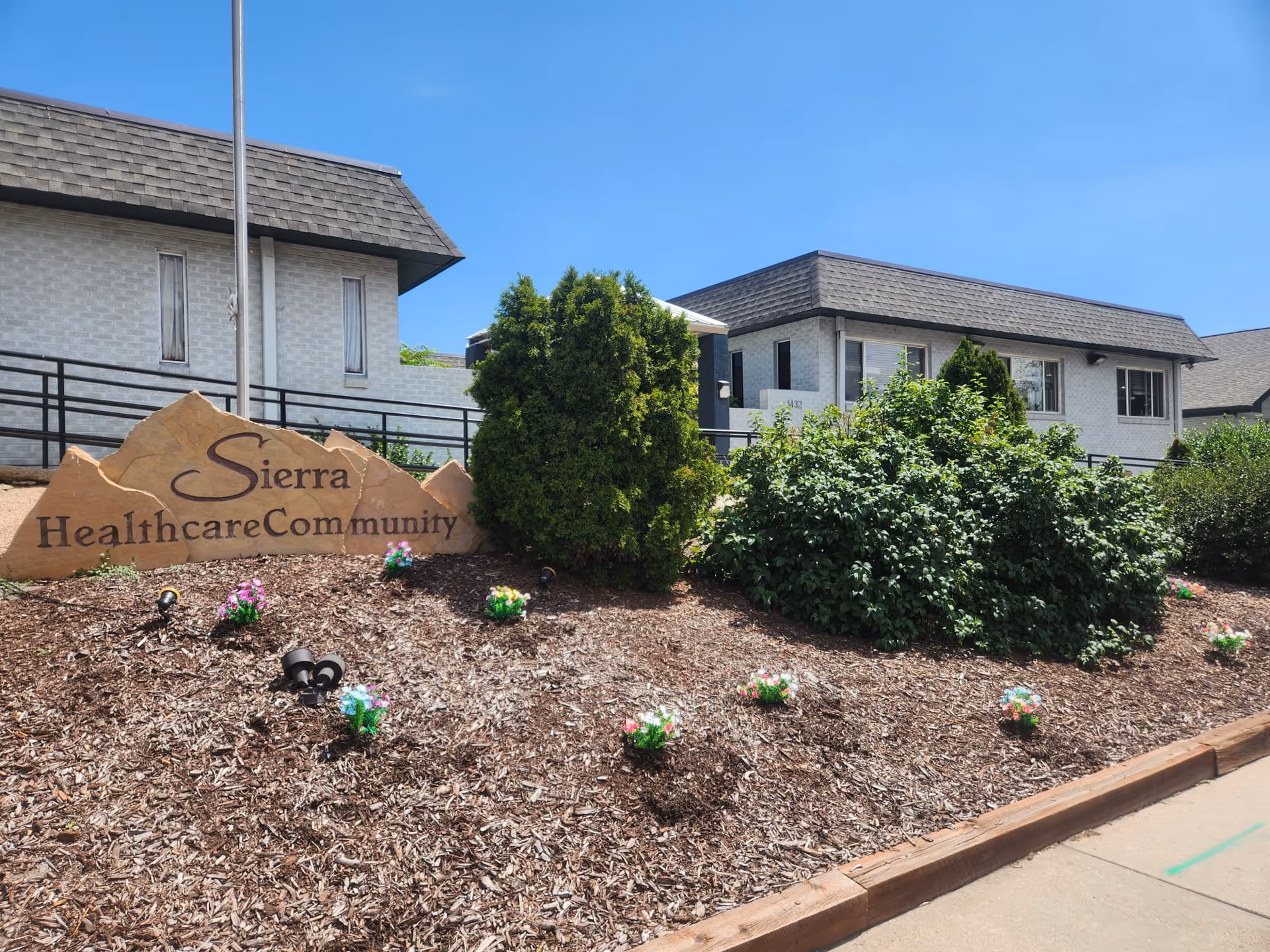Exterior view of a senior living facility with a stone sign reading 'Sierra Healthcare Community' and landscaped front yard.