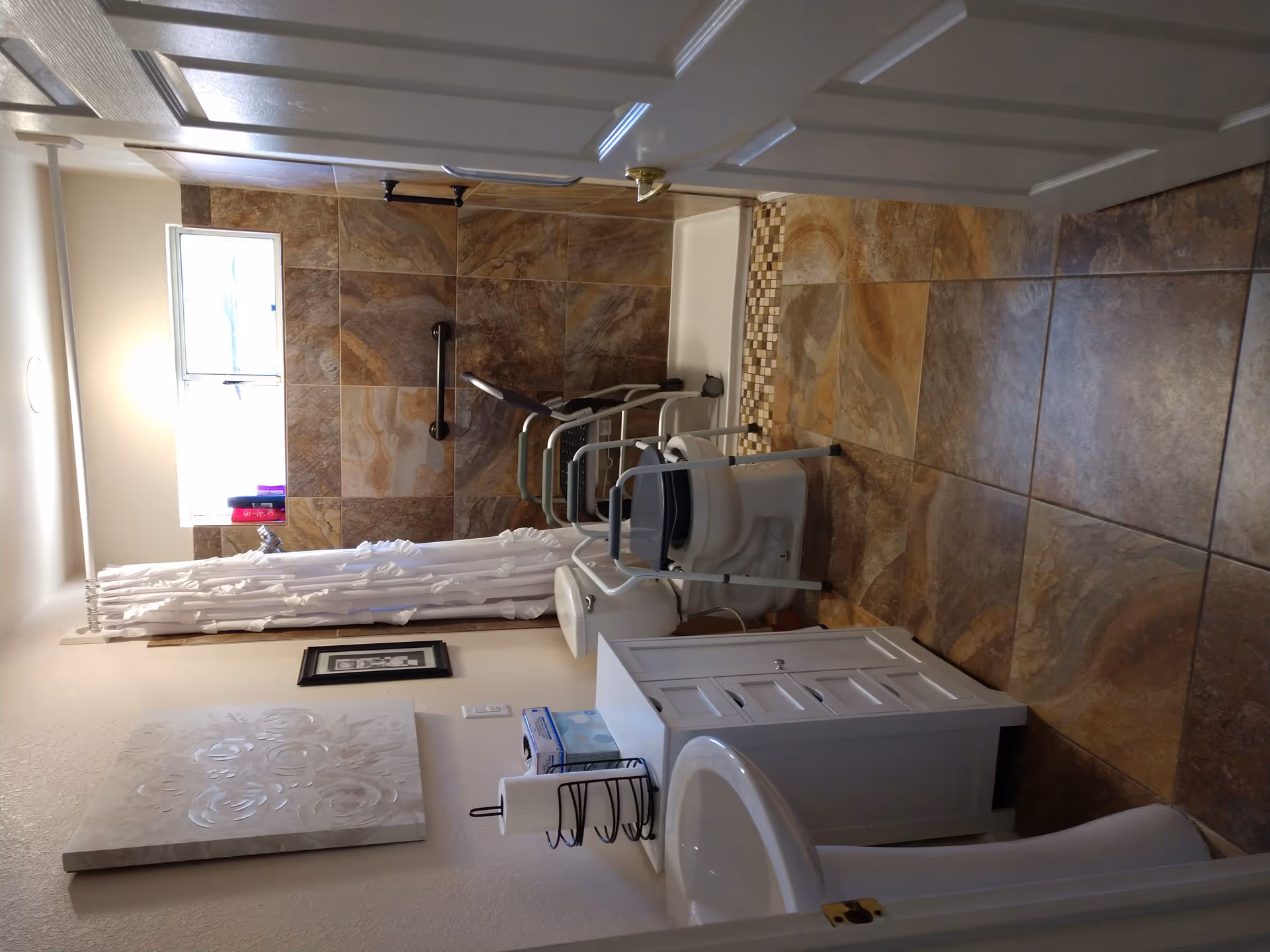 Bathroom with a tiled walk-in shower, shower chair, grab bars, toilet, and vanity.