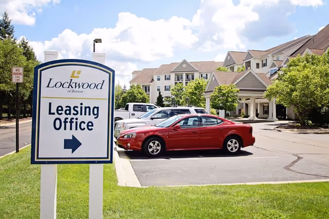 Sign reading 'Lockwood Leasing Office' in front of the Lockwood of Burton building and parking lot with parked cars.