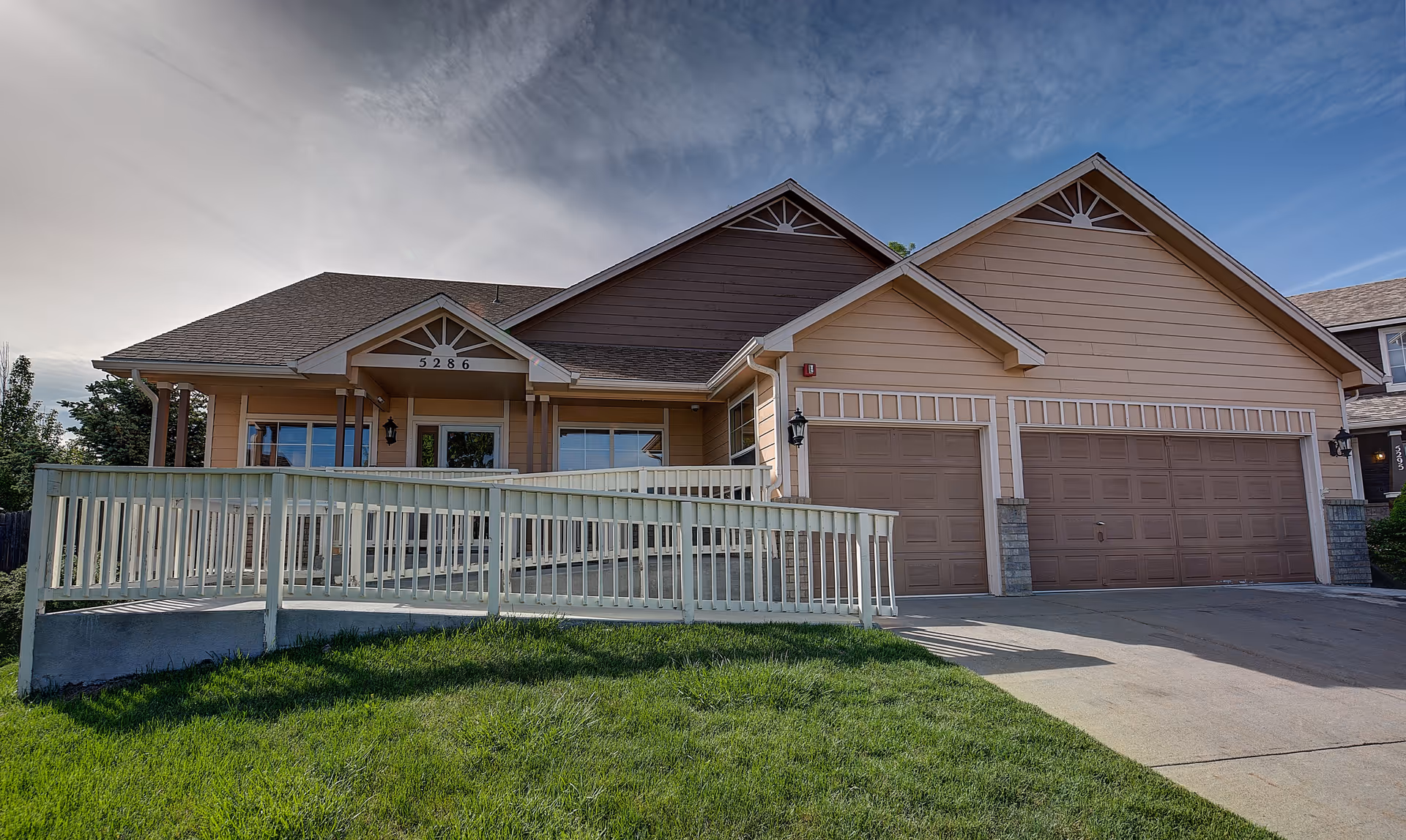 Front exterior of a single-story residential building with a porch, wheelchair ramp, and three-car garage.