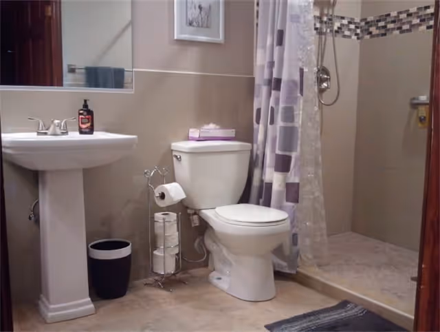 Bathroom with pedestal sink, toilet, a toilet-paper stand, and a walk-in shower with a patterned curtain.